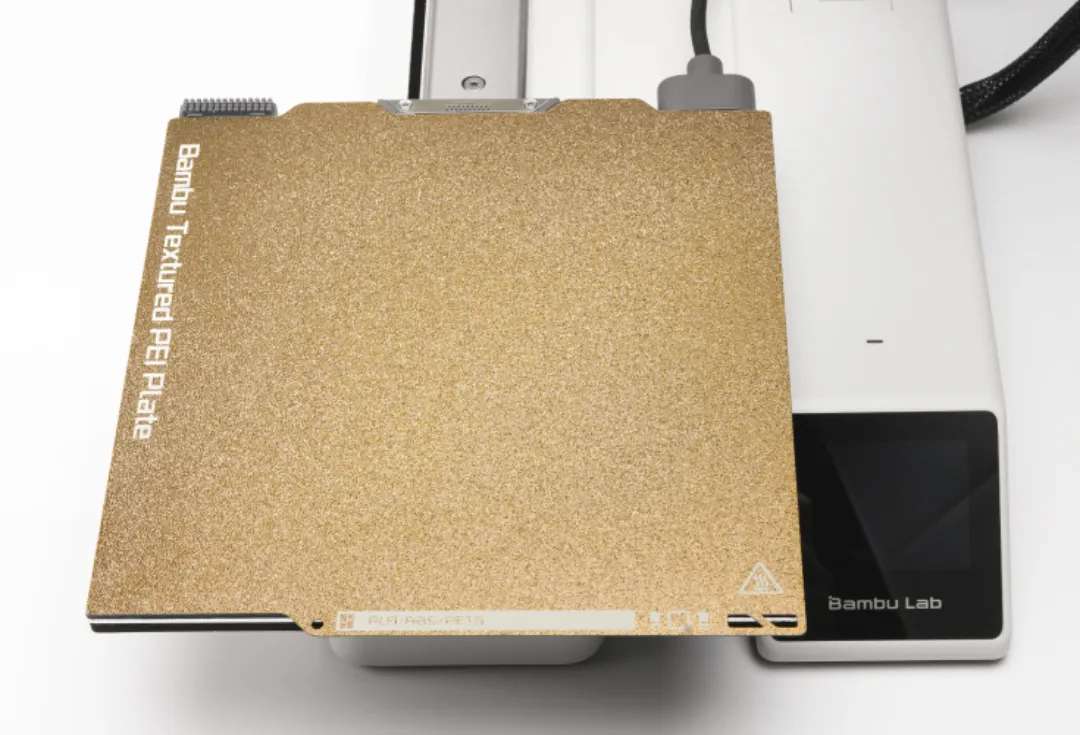 Процес встановлення золотистої Bambu Lab Textured PEI Plate A1 mini на магнітний підігрівальний стіл 3D-принтера, забезпечуючи щільне прилягання.